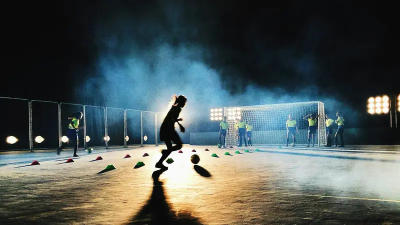 A goalkeeper training under floodlights on a wet pitch at night